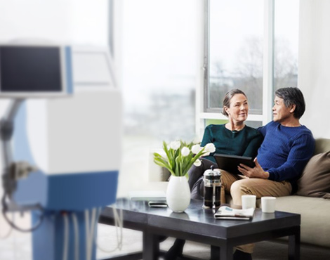 A woman and man sitting on a couch with a home haemodialysis device